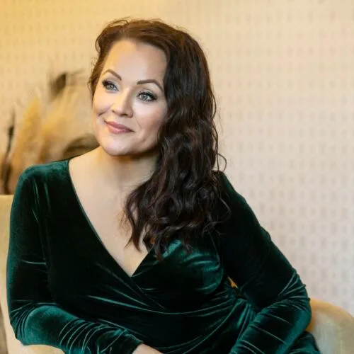 Heid Pakarinen is leaning back in a sofa chair wearing a green velvet skirt.