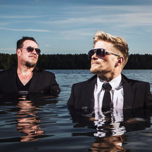 Käsityöläiset-bändin Mika Ikonen ja Anssi Häkkinen seisovat järvessä.
