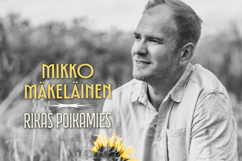Mikko Mäkeläinen istuu viljapellossa auringonkukkia kädessään.