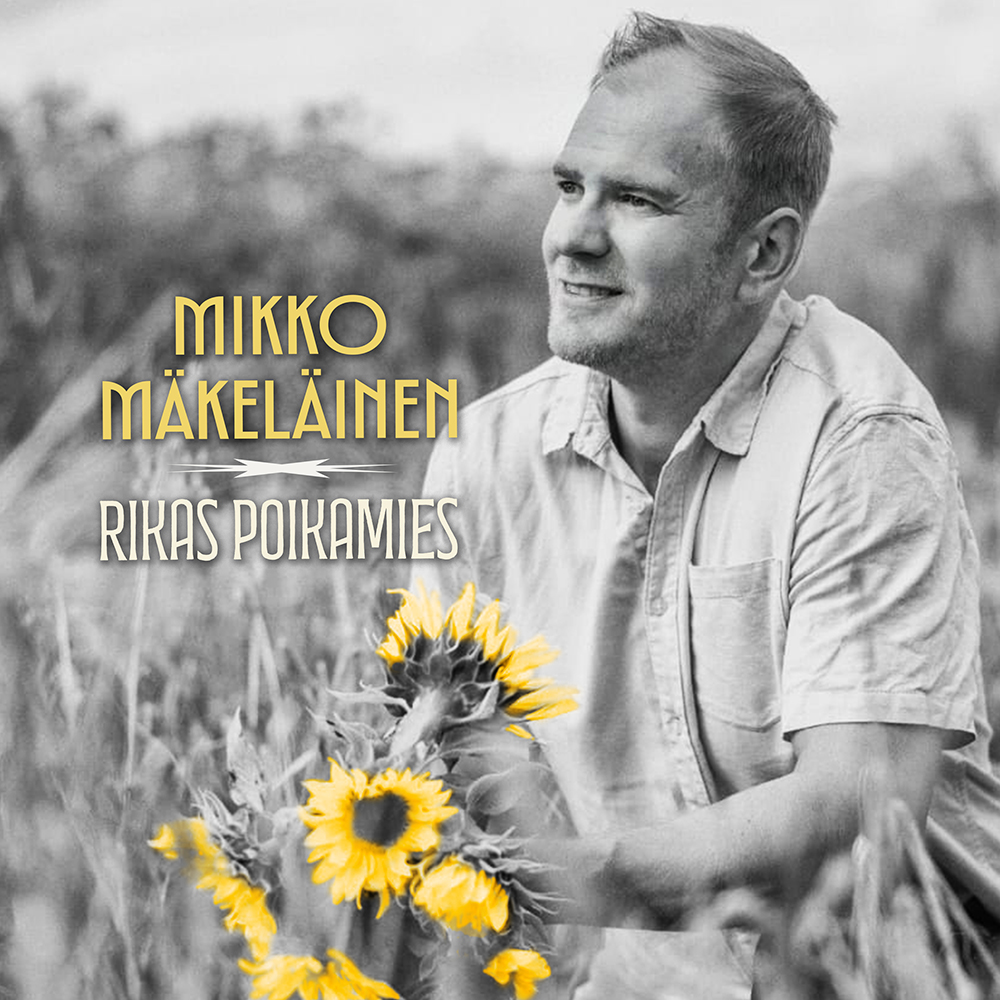 Mikko Mäkeläinen istuu viljapellossa auringonkukkia kädessään.