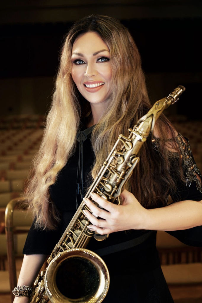 Vaaleatukkainen SIni Sax saksofoninsa kanssa.