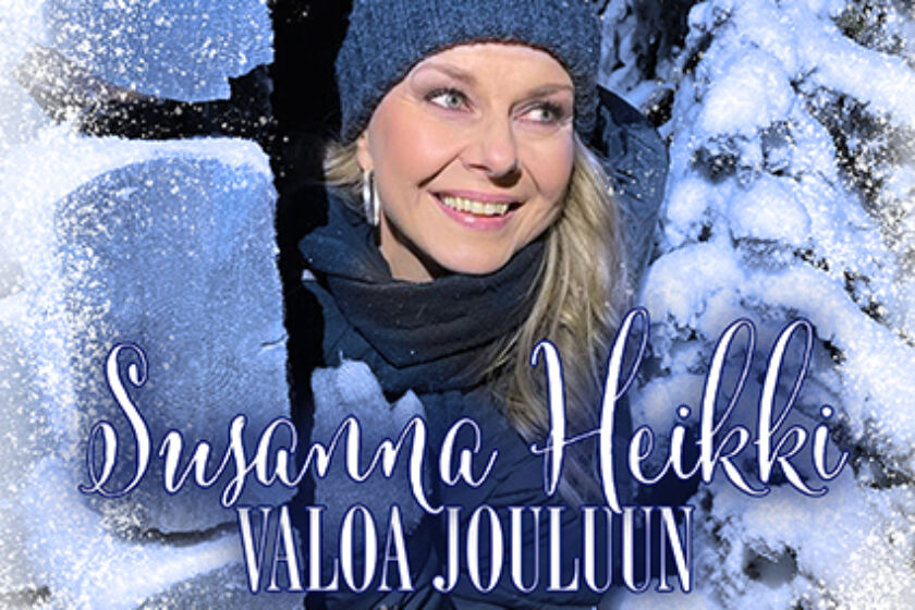 Susanna Heikki kurkkaa huurteisen hirsivajan kulmalta. Taustalla on lumisia kuusia.